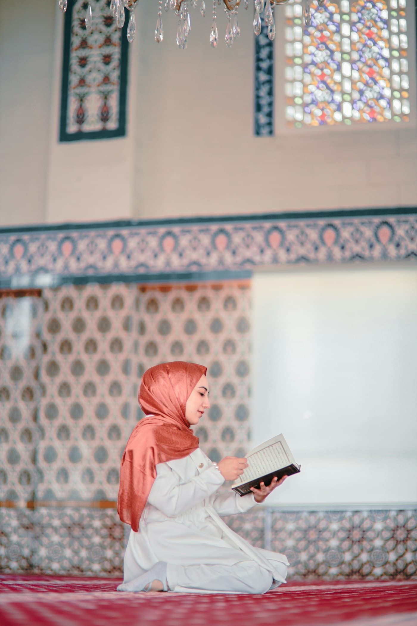 A young girl in a red hijab reading the Quran inside a mosque