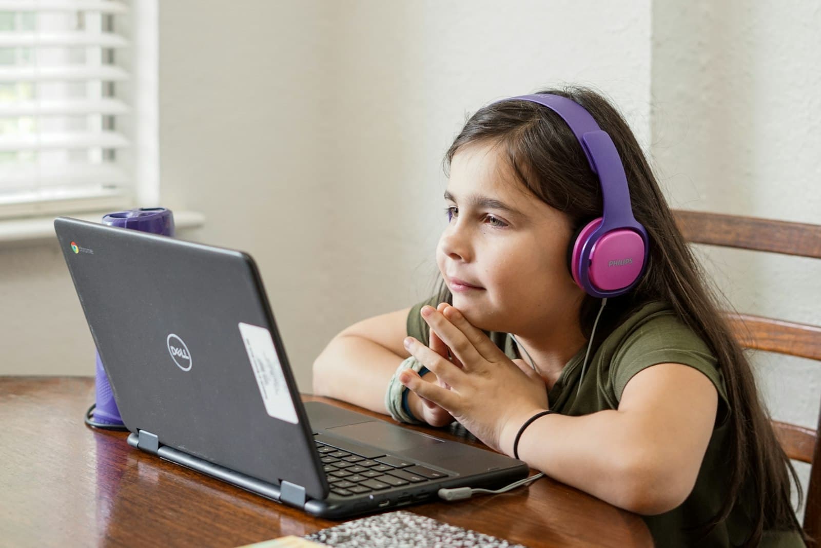 A young girl wearing headphones smiling during an online class on her laptop