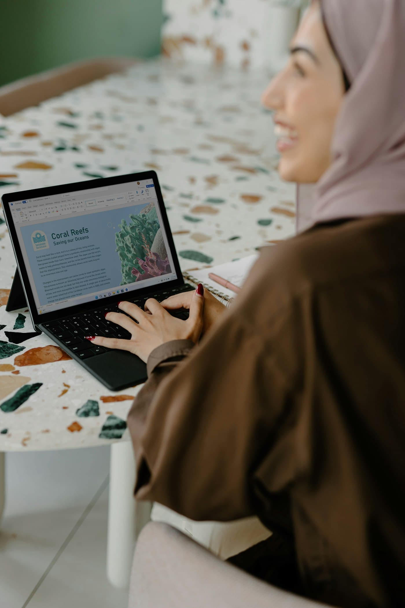 A smiling student in hijab taking an online class on a laptop
